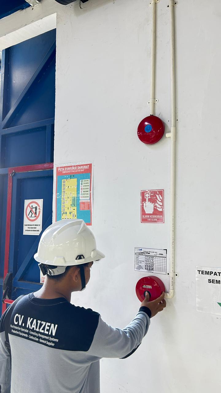 Teknisi berhelm menekan tombol manual call point alarm kebakaran pada dinding fasilitas